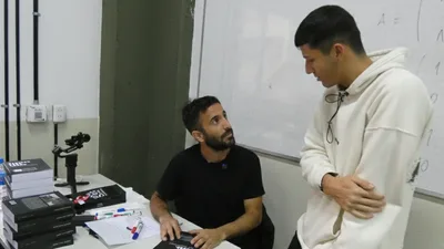 Juani conversando con un estudiante junto a una pila de sus libros